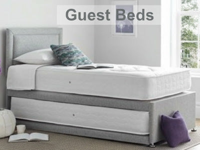 Gray guest bed in a room with a window and decor elements.