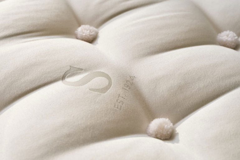 Close-up of a tufted white cushion with pom-poms and a brand logo.