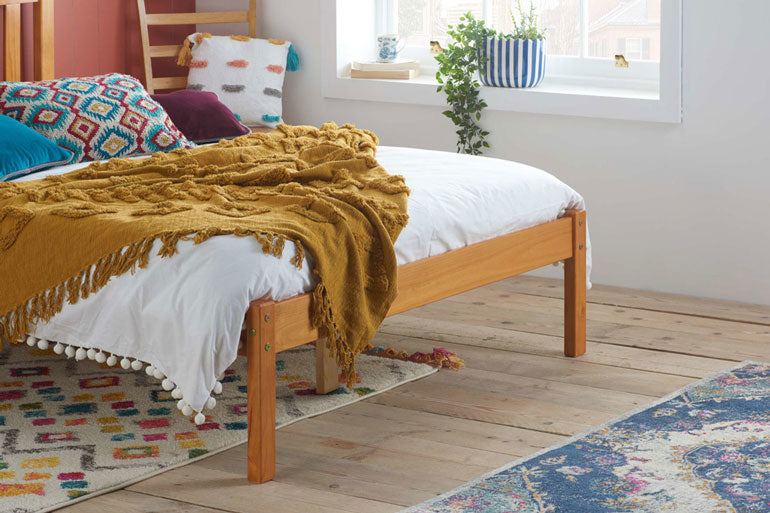 Wooden bed with a mustard yellow blanket in a room with a window and rug.