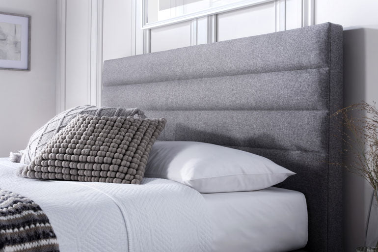Kaydian Appleford Ottoman Headboard with pillows and a blanket in a bedroom setting.