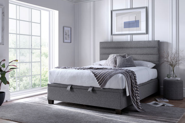 Kaydian Appleford Ottoman Bed in Marbella Grey in a modern bedroom with large windows.