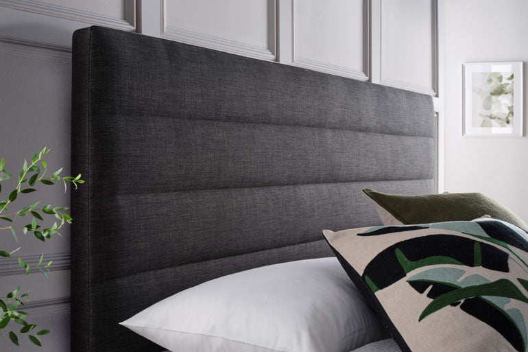 Close-up of Kaydian Appleford Ottoman headboard in slate with decorative pillows.