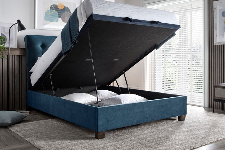 Kaydian Ashbrooke Ottoman Bed in Vogue Ocean with storage compartment open in a room with large windows.