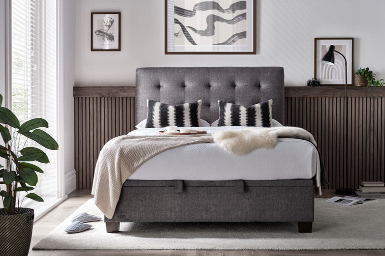 Kaydian Ashbrooke Ottoman bed in Vogue Grey with striped pillows in a bedroom setting.