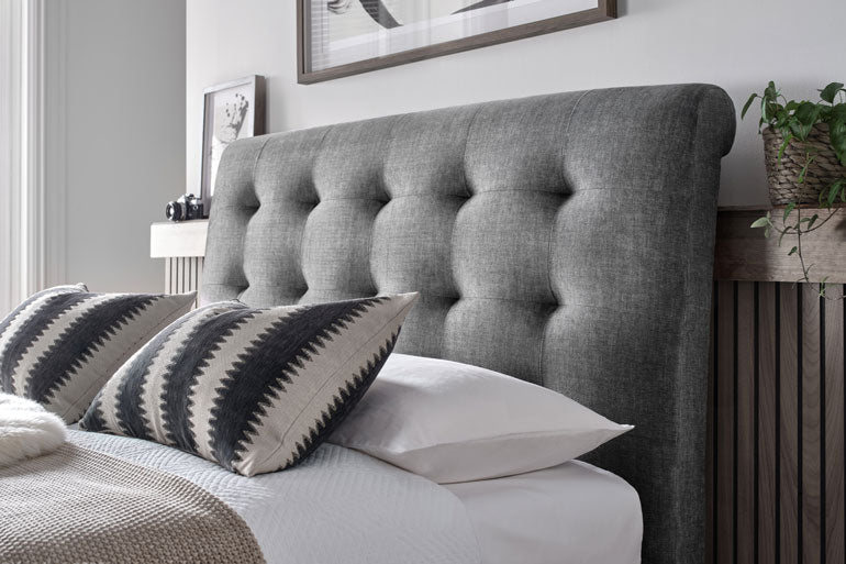 Close-up of Kaydian Ashbrooke Ottoman headboard with patterned pillows on a bed in a bedroom setting.