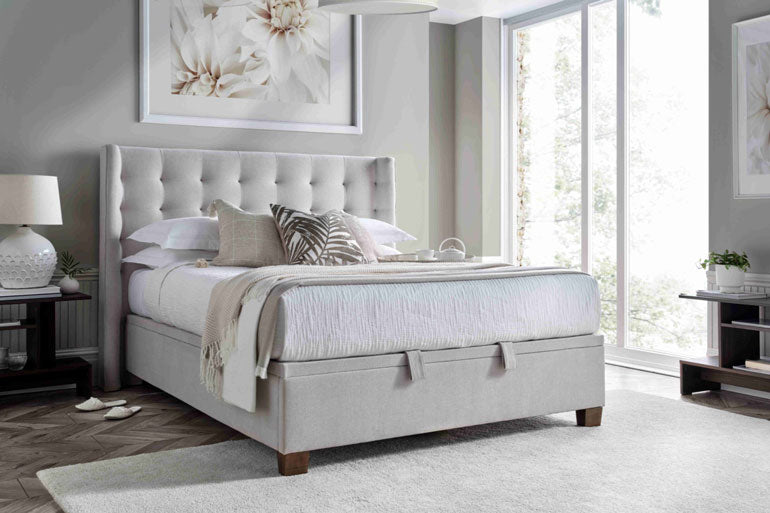 Kaydian Brunton Ottoman Bed in Maskat Clay in beige bedroom setting with bedside and rug.