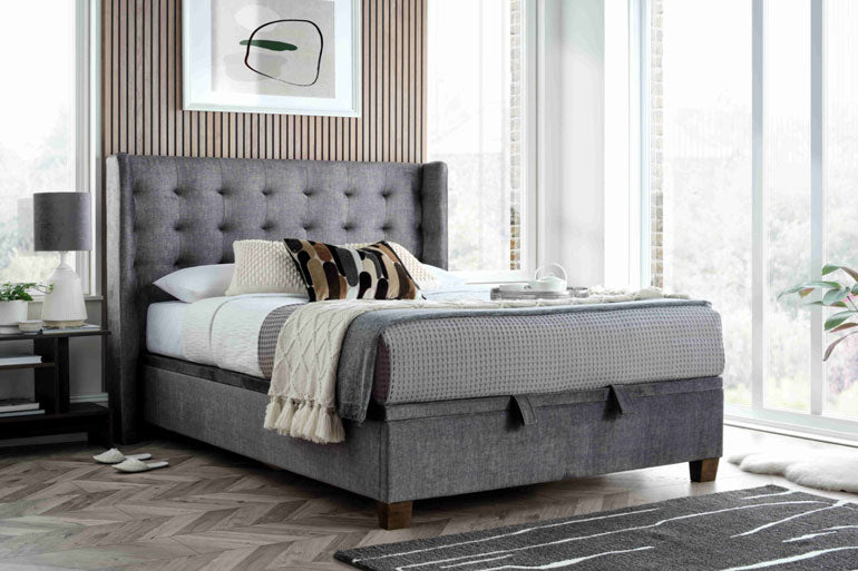 Kaydian Brunton Ottoman Bed in Vogue Grey in bedroom with wooden floor, rug and bedside.