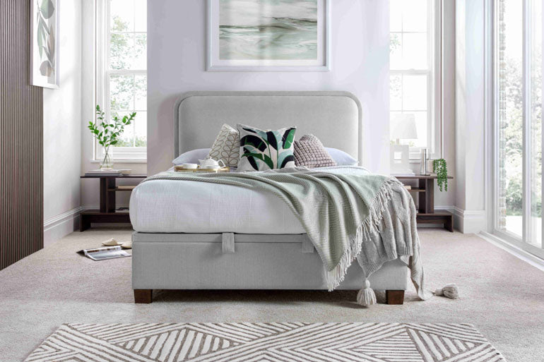 A Kaydian Clifton Ottoman Bed in Maskat Clay with a high headboard, low foot end, and wooden legs in a bedroom setting.