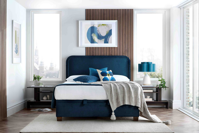 Kaydian Clifton Ottoman Bed in Vogue Ocean, in bedroom featuring decorative pillows and a throw blanket.