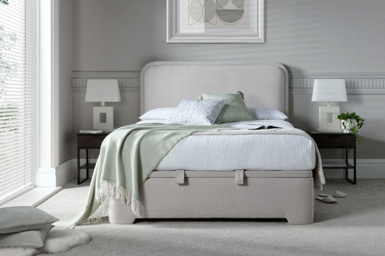 Neatly made Kaydian Clitheroe Ottoman Bed with light gray bedding and green blanket in a bedroom setting.