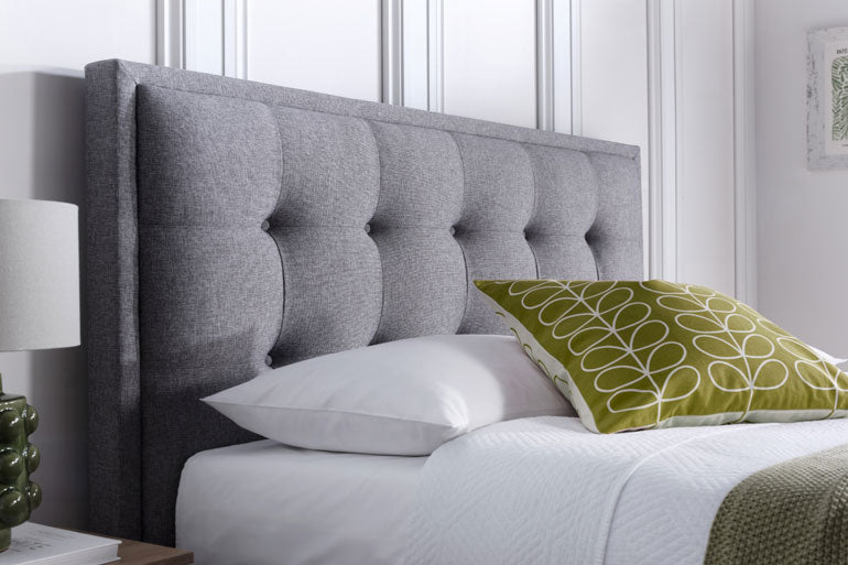 Kaydian Falfield Ottoman headboard in Marbella Grey with white pillows and a green pillow with a pattern on a bed.