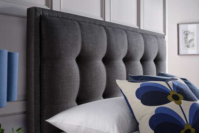 Kaydian upholstered Falfield Ottoman headboard with white and floral-patterned pillows in a bedroom setting.