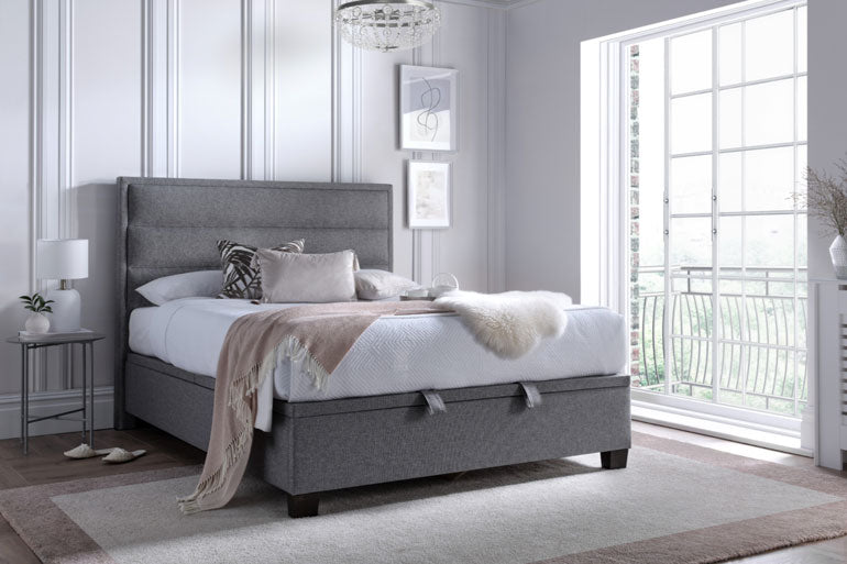 Kaydian Kirkland Ottoman Bed in Marbella Grey in a modern bedroom with large windows.