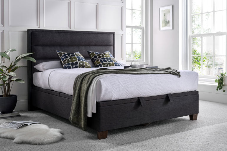 Bedroom with a Kaydian Kirkland Ottoman Bed in Slate featuring a dark upholstered headboard and white bedding.