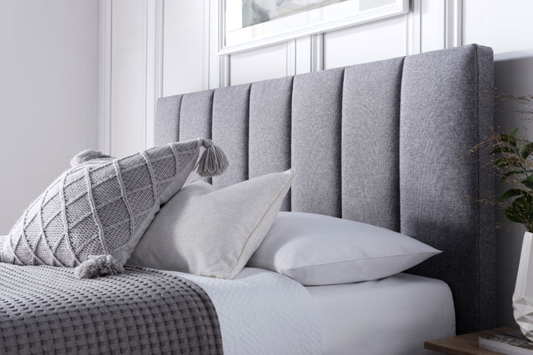 Close-up of Kaydian Medlam Ottoman headboard in Marbella Grey with pillows on a bed in a bedroom setting.
