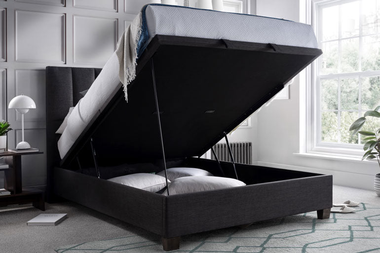 Kaydian Medlam Ottoman Bed in Slate with storage compartment in a room with a window and lamp.