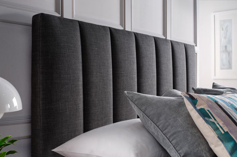 Close-up of Kaydian Medlam Ottoman headboard in Slate with pillows in a bedroom setting.