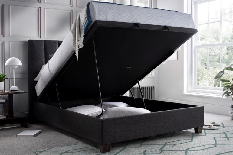 Kaydian Medlam Ottoman Bed in Slate with storage compartment open in a room with large windows.