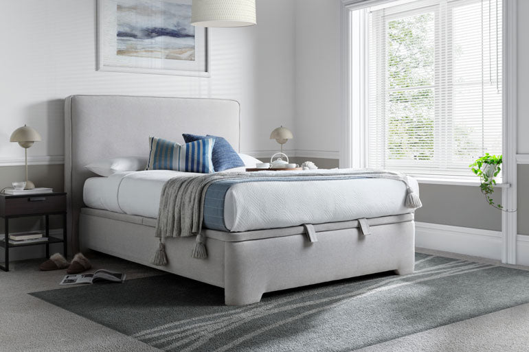Modern bedroom with a Kaydian Newland Ottoman bed, striped pillows, and a side table.