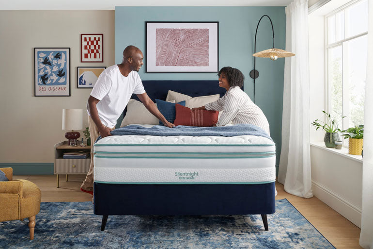 Two people adjusting a Silentnight UltraGel 3000 Boxtop mattress in a bedroom with decor elements.