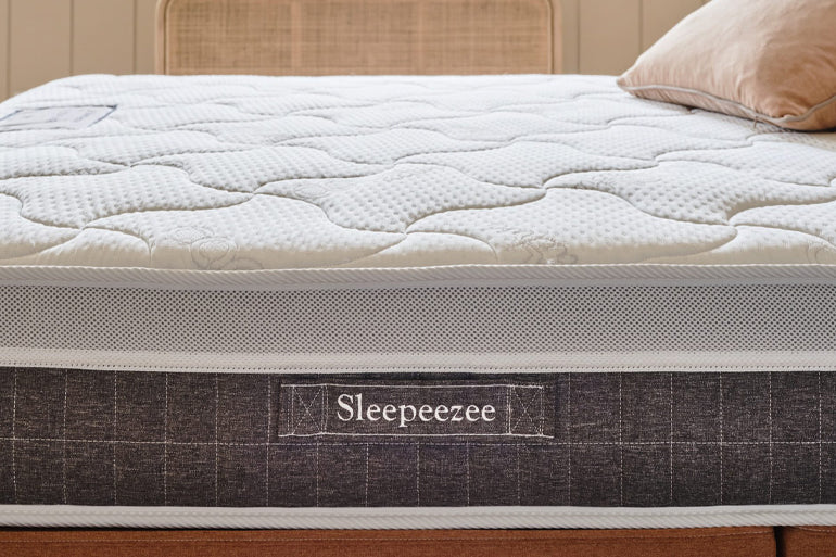 Sleepeezee mattress on a bed with a wooden headboard and beige pillow.