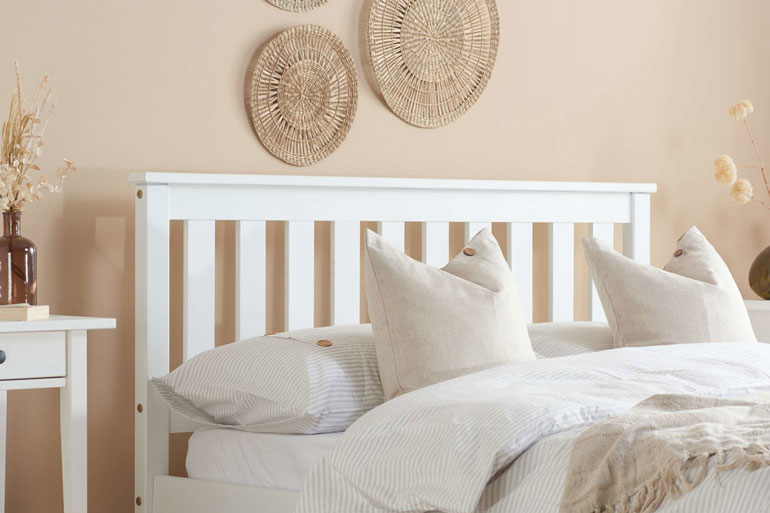 Close-up of Birlea Denver bed in white with pillows against a beige wall with decorative circular wall hangings.