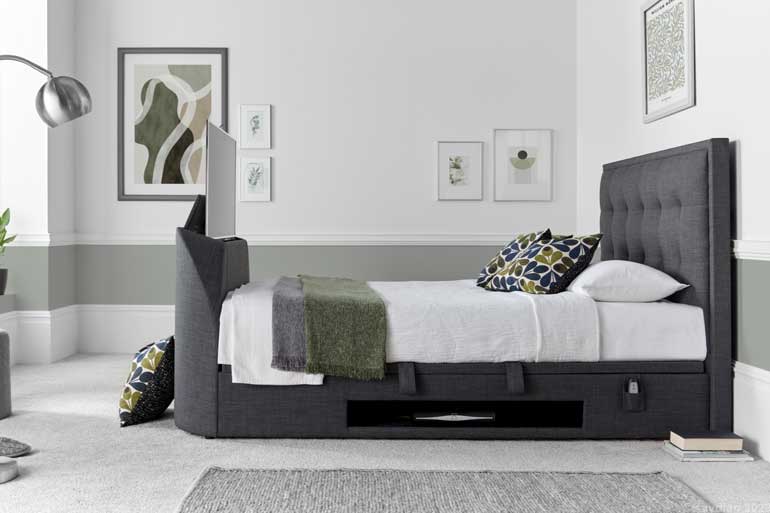 Side view of Kaydian Falstone | Falmer TV Ottoman Bed in Slate with TV compartment open and bedroom setting.