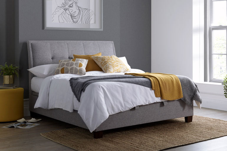 Kaydian Accent Ottoman Bed in Marbella Grey in bedroom setting with white bedding.
