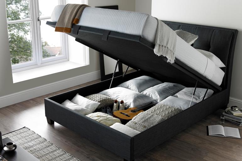 Kaydian Accent Ottoman Bed in Slate with storage compartment open and bedding inside.